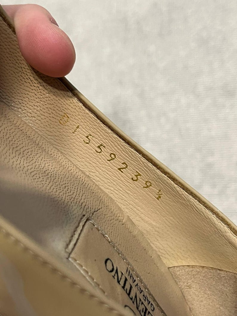 Puede incluir: Primer plano del interior de un zapato de cuero beige. La plantilla del zapato muestra el n&uacute;mero "31559239 1/2" en letras doradas. La marca "Valentino Garavani" es visible.