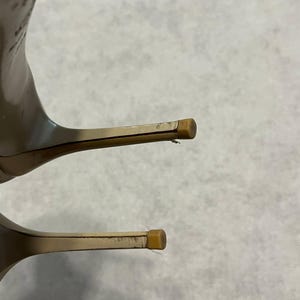 Puede incluir: Primer plano de dos zapatos de tac&oacute;n alto. Los tacones son de color beige claro con un dise&ntilde;o fino y de aguja. Las puntas de los tacones tienen una peque&ntilde;a tapa cuadrada de color marr&oacute;n claro. Los zapatos parecen estar hechos de un material liso.