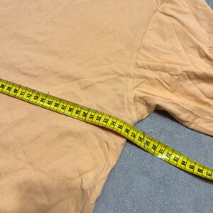 May include: A light orange long-sleeved shirt with a yellow measuring tape laid across it. The tape shows measurements in inches, starting at 38 inches and extending to 67 inches.