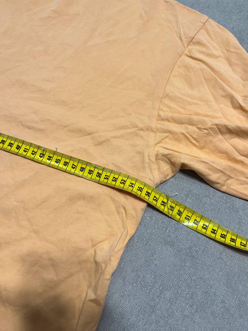 May include: A light orange long-sleeved shirt with a yellow measuring tape laid across it. The tape shows measurements in inches, starting at 38 inches and extending to 67 inches.