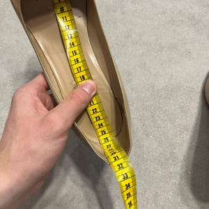 Puede incluir: Un zapato plano beige de mujer se mide con una cinta m&eacute;trica amarilla. La cinta muestra una medida de aproximadamente 45 cm. El zapato tiene una punta redondeada y un tac&oacute;n bajo. El interior del zapato es de color beige claro.