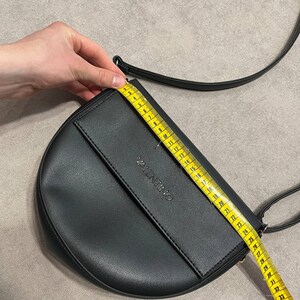 May include: Black Valentino crossbody bag with a flap closure and a long strap. The bag is measured with a tape measure, showing a length of approximately 14 inches. The word "VALENTINO" is embossed on the front.