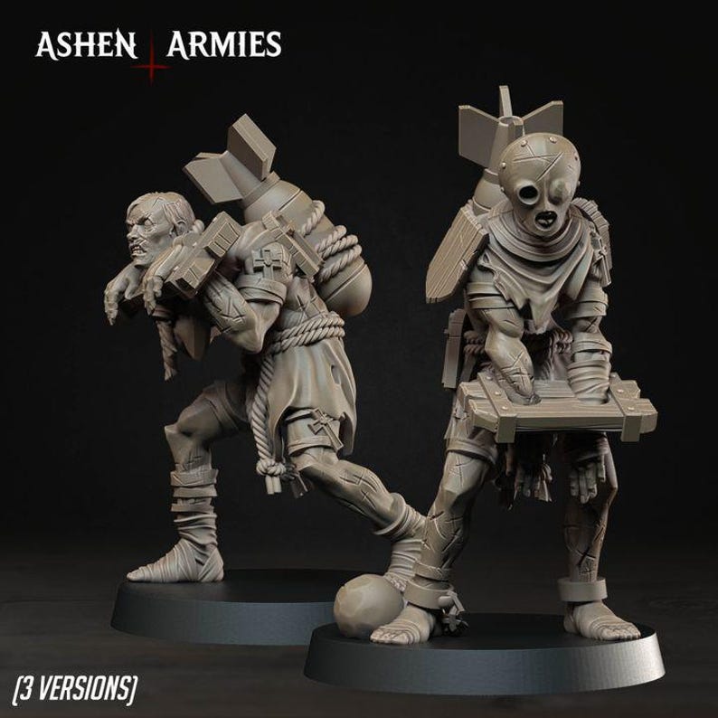 May include: Two grey resin miniature figures from Ashen Armies. One figure wears a mask and carries a large bomb on its back, while the other has a visible face and carries a bomb. Both figures stand on circular bases with detailed clothing.