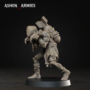 May include: A grey unpainted miniature figure from Ashen Armies, depicting a hunched character carrying a large bomb on their back secured with rope. The figure wears tattered clothing, leg wraps, and a mask, standing on a circular black base.