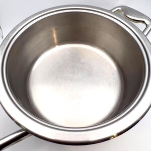 May include: A stainless steel cooking pot with two handles. The pot has a wide, round body and a shiny, reflective surface. The handles are curved and attached to the sides of the pot. The pot is designed for cooking.