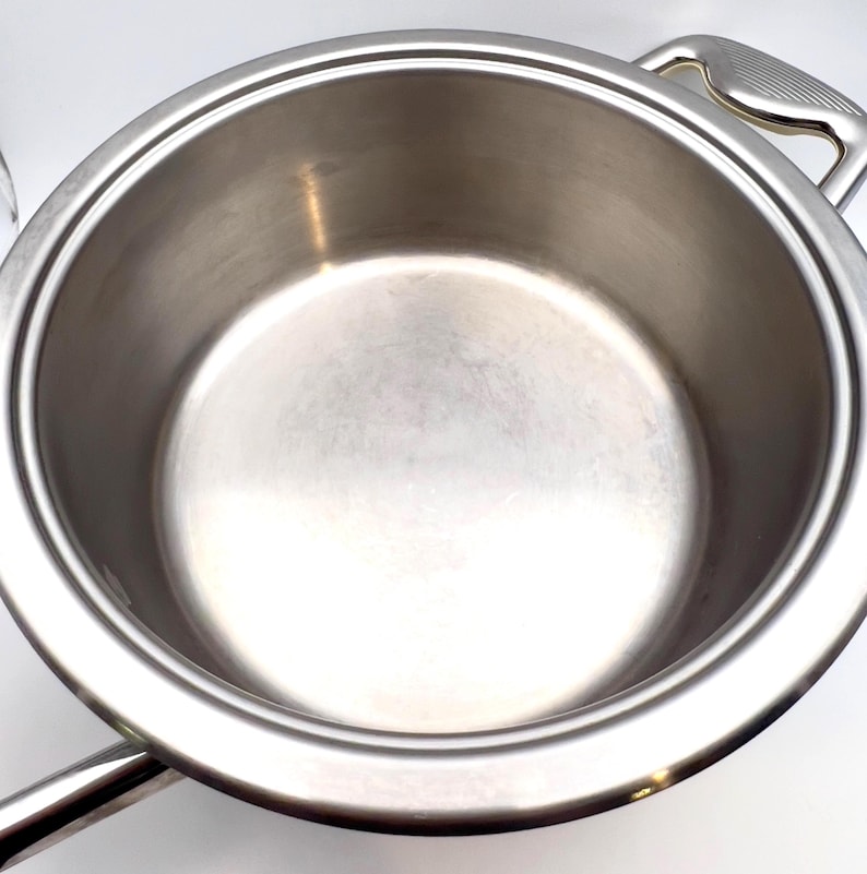 May include: A stainless steel cooking pot with two handles. The pot has a wide, round body and a shiny, reflective surface. The handles are curved and attached to the sides of the pot. The pot is designed for cooking.