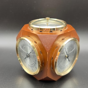 May include: A wooden weather station with a brass-colored bezel. The station has three analog gauges and a compass. The gauges display temperature and humidity readings. The wooden body is a dark brown color.