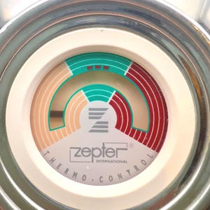 May include: Close-up of a Zepter Thermo Control dial. The dial features a white face with a circular design in shades of green, red, and beige. The text "zepter INTERNATIONAL THERMO.CONTROL" is printed on the dial.