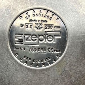 May include: Close-up of a stainless steel Zepter product base. The base features embossed text including "Made in Italy", "3.0 L", and "200 mm". Other text includes "USP 5154311 GUARANTEE".
