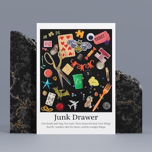 以下が含まれることがあります： 「Junk Drawer」と題されたプリントで、ハサミ、トランプ、おもちゃの飛行機、犬の置物など、さまざまな小さなオブジェクトが特徴です。下部のテキストには「One lonely lady bug. Two stars. Three times the luck, Four things that fly, Number nine five times, and Six oranges things.」と書かれています。