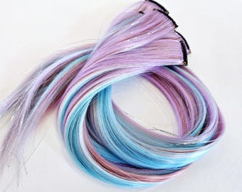May include: A set of clip-in hair extensions featuring a blend of light blue, pink, and white strands. The hair extensions have a shimmering finish.