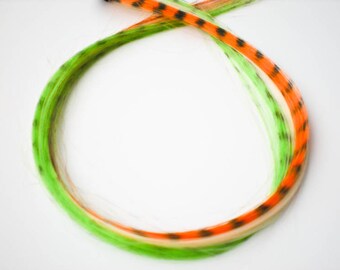 Könnte beinhalten: Ein Set mit drei Haarverlängerungen in Grün, Orange und Weiß mit schwarzen Punkten. Die Extensions bestehen aus synthetischem Haar und sind dazu bestimmt, für eine vorübergehende Veränderung des Stils zu Ihrem eigenen Haar hinzugefügt zu werden.