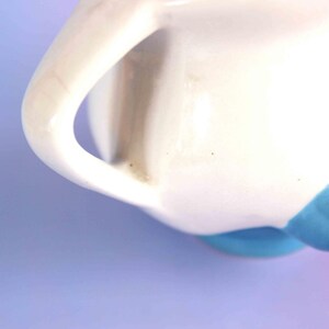 May include: A white ceramic pitcher featuring a curved handle and a smooth, glossy finish. The base of the pitcher is accented with a vibrant blue glaze, creating a distinct contrast against the white body. The design is simple and functional.