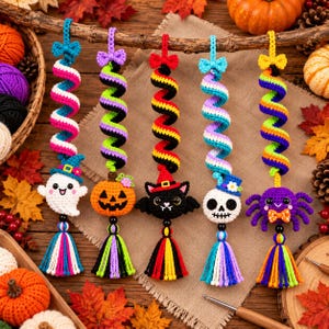 May include: Five hanging crochet ornaments featuring spiral designs in various colors. The ornaments include a white ghost, an orange pumpkin, a black cat, a white skull, and a purple spider, each topped with a small bow and finished with a tassel.