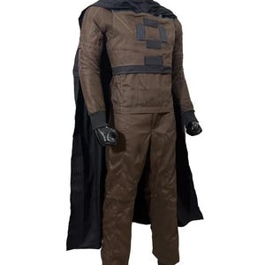 May include: A brown costume with a black cape, gloves, and a head covering. The costume features a jacket with square patches and a matching pair of pants. The outfit is displayed on a mannequin.