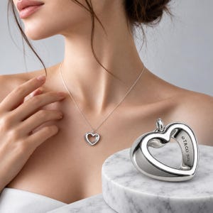 Puede incluir: Un collar con colgante de corazón en plata de ley con un diseño de corazón abierto pulido. El colgante cuelga de una cadena delicada. Se ve un dije de corazón a juego, grabado con el texto T&CO 925 en su superficie lateral.