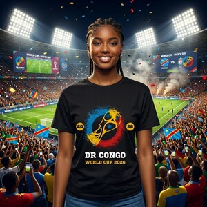 May include: A black t-shirt featuring a graphic of a gold trophy inside a blue and red circular brushstroke design. The text 20 and 26 are on either side of the graphic, with DR CONGO and WORLD CUP 2026 printed in white and yellow below.