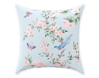 May include: A light blue throw pillow with a floral pattern featuring pink flowers, green leaves, and blue birds. The pillow has a square shape and a soft, comfortable texture.