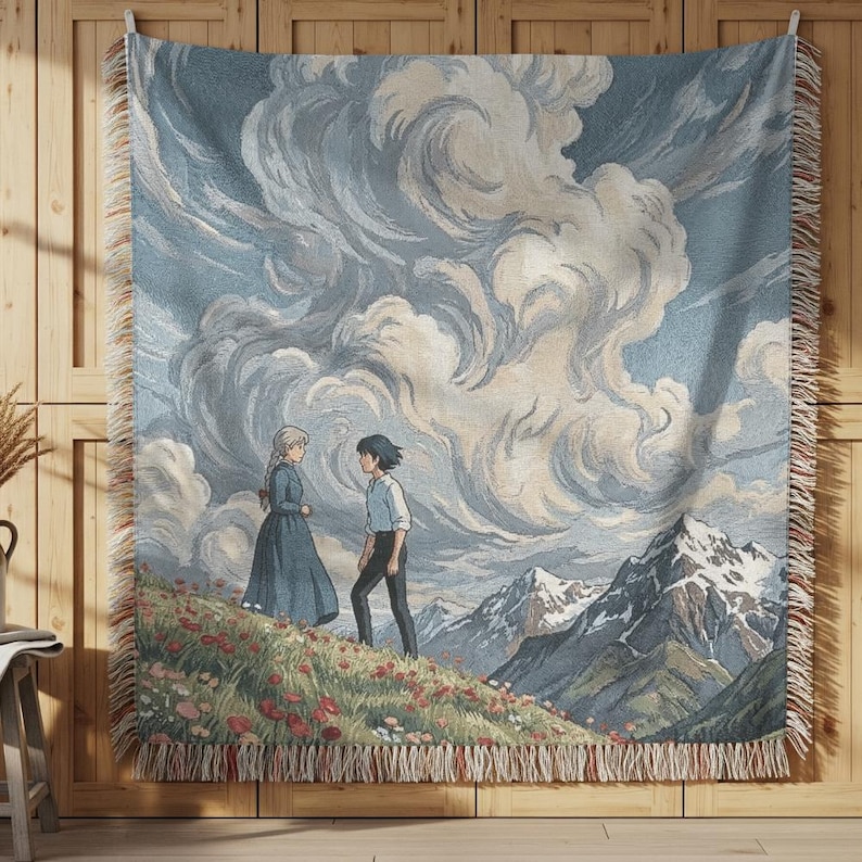 May include: A woven tapestry throw blanket featuring a scene with two figures on a flowered hillside, with mountains in the background and a cloudy sky. The blanket has a fringed edge and is primarily blue, white, and beige.