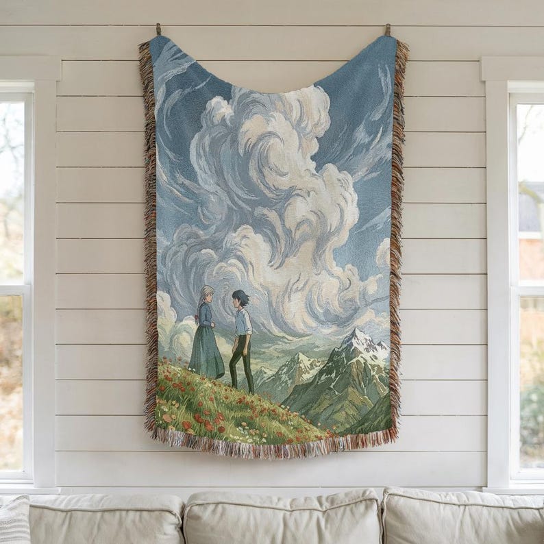 May include: Woven tapestry featuring a scenic landscape with two figures on a flowered hillside, mountains, and a cloudy sky. The tapestry has a blue and beige color scheme with fringed edges, hung on a white wall.