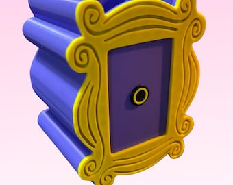 Op de afbeelding: Een paars en geel decoratief frame, dat doet denken aan een tv-programma, wordt getoond. Het frame heeft een gele rand met sierlijke krullen en een paars interieur. Het frame is gemonteerd op een paars doosvormige container, ideaal voor het bewaren van kleine items.