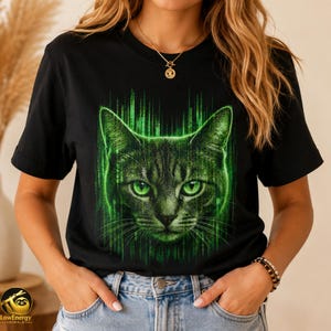 May include: A black short-sleeved t-shirt featuring a graphic print of a cat's face centered on the chest. The cat is rendered in shades of green with a digital matrix-style background effect consisting of vertical lines of code.