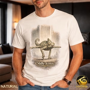 Può includere: T-shirt bianco con un'illustrazione dettagliata di un camaleonte. Il design include il testo "Oddly Iconic". La maglietta è realizzata in un materiale morbido. Il camaleonte è raffigurato con gli arti distesi.
