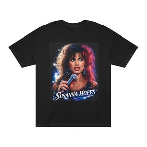May include: Black t-shirt featuring a graphic of Susanna Hoffs holding a microphone. The image has a stage-like background with blue and red lighting and the text "Susanna Hoffs" in a stylized font.