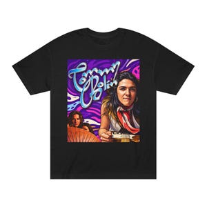 Könnte beinhalten: Schwarzes T-Shirt mit einer farbenfrohen Grafik einer Frau, die Gitarre spielt, mit dem Namen "Tommy Bolin" in einer stilisierten Schriftart. Das Design hat einen lebendigen lila und blauen Hintergrund im psychedelischen Stil.