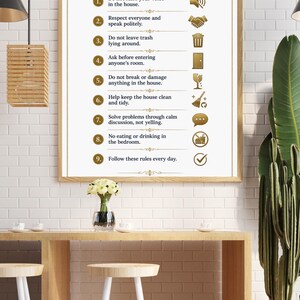 May include: A framed sign with the words "HOUSE RULES" at the top. The sign lists nine rules in gold text with corresponding icons. The rules include speaking politely, keeping the house clean, and solving problems calmly. The sign is hanging above a wooden table.