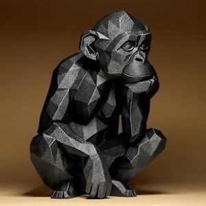 May include: A black geometric sculpture of a monkey in a seated position, resting its chin on its hand. The sculpture has a faceted design, giving it a modern, angular appearance. The monkey's facial features are detailed, and the overall aesthetic is minimalist.