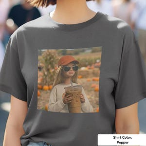 May include: Pepper-colored t-shirt featuring a graphic of a person wearing sunglasses and a cap, holding an iced coffee. The graphic is set against a pumpkin patch backdrop. The shirt color is pepper.