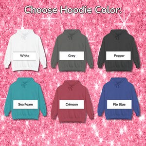 May include: A color chart displaying six hooded sweatshirts with the text Choose Hoodie Color at the top. The hoodies are white, grey, pepper, sea foam, crimson, and flo blue. Each hoodie features a rectangular label with its respective color name.