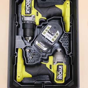 May include: A black and yellow Ryobi power tool set in a black case. The set includes a drill, impact driver, and battery. The tools are arranged in a custom-fit interior, providing secure storage and organization for the tools.