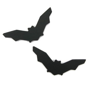 Puede incluir: Dos murciélagos de papel negro, recortados en una forma de silueta simple, sobre un fondo blanco.