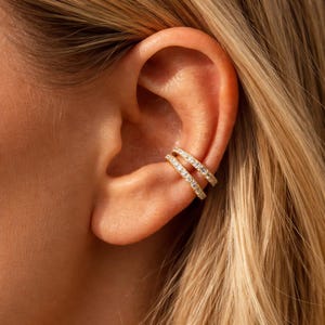 May include: A set of three ceramic mugs with a speckled, matte finish. The mugs are in shades of cream, light brown, and dark brown. Each mug has a simple, minimalist design and a rounded handle.