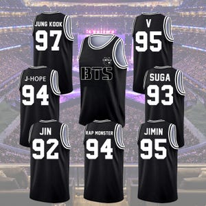 Puede incluir: Camisetas de baloncesto negras con ribetes y letras blancas. Las camisetas presentan los nombres y números de los miembros de BTS: Jung Kook (97), V (95), J-Hope (94), Suga (93), Jin (92), Rap Monster (94) y Jimin (95). La camiseta central muestra el logotipo de BTS.