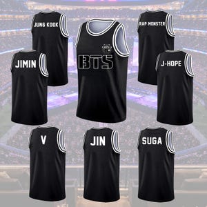 May include: Black basketball jerseys with white trim and lettering. The jerseys feature the word "BTS" and individual names like "JUNG KOOK", "JIMIN", "RAP MONSTER", "J-HOPE", "V", "JIN", and "SUGA".