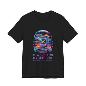 May include: Black t-shirt featuring a colorful graphic of a retro computer with the word "OK" on the screen, surrounded by flames. The text "IT WORKS ON MY MACHINE" and "DEPLOYMENT STATUS: IRRELEVANT" are below the graphic.