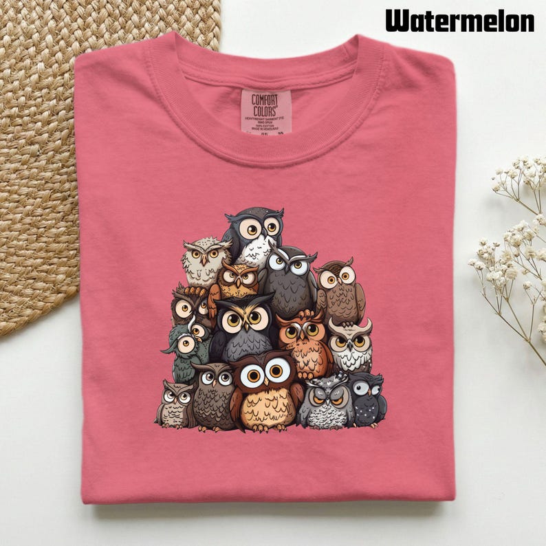 Puede incluir: Una camiseta de cuello redondo color sand&iacute;a con un estampado gr&aacute;fico de un gran grupo de b&uacute;hos variados en tonos marrones, grises y blancos. La camiseta tiene una etiqueta de la marca Comfort Colors en el cuello interior y el texto Watermelon.