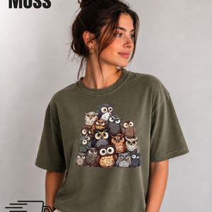 Puede incluir: Una camiseta de manga corta color verde musgo con un estampado gr&aacute;fico de un grupo de varios b&uacute;hos en tonos marrones, grises y blancos. La palabra Moss est&aacute; impresa en negro en la esquina superior izquierda y un icono de cami&oacute;n negro abajo.