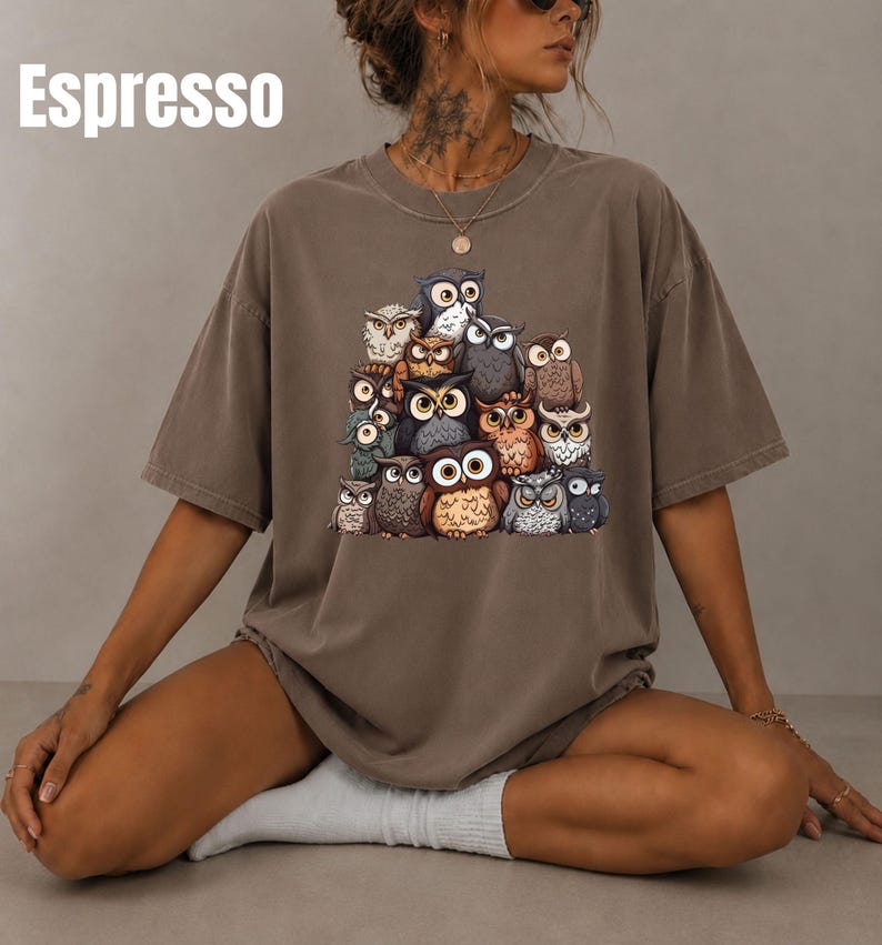 Puede incluir: Una camiseta de manga corta color espresso con un estampado gr&aacute;fico de un grupo de varios b&uacute;hos en tonos marrones, grises y blancos. La palabra Espresso est&aacute; impresa en blanco en la esquina superior izquierda de la prenda.