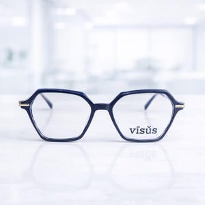 Op de afbeelding: Donker marineblauwe bril met een geometrisch zeshoekig montuur. De bril heeft dunne pootjes en de merknaam "visus" is op het rechterglas gedrukt. Het montuur heeft gouden accenten.