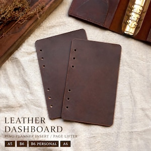 Könnte beinhalten: Zwei dunkelbraune Leder-Dashboard-Einsätze für Ringplaner. Die Einsätze haben abgerundete Ecken und vorgestanzte Löcher zum Binden. Der Text "LEATHER DASHBOARD" und "RING PLANNER INSERT / PAGE LIFTER" ist sichtbar, zusammen mit Größenoptionen.