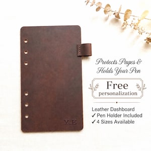 May include: A dark brown leather dashboard featuring six punched holes along the left edge and a small pen holder loop on the right side. The text "Y.E" is embossed at the bottom. Text on the right reads: "Protects Pages & Holds Your Pen", "Free personalisation", "Leather Dashboard", "Pen Holder Included", and "4 Sizes Available".