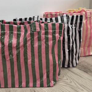 Puede incluir: Cuatro bolsas de mano con rayas verticales en varios colores: rosa y verde, blanco y negro, rosa y blanco y amarillo. Las bolsas tienen un acabado brillante y forma rectangular con asas.