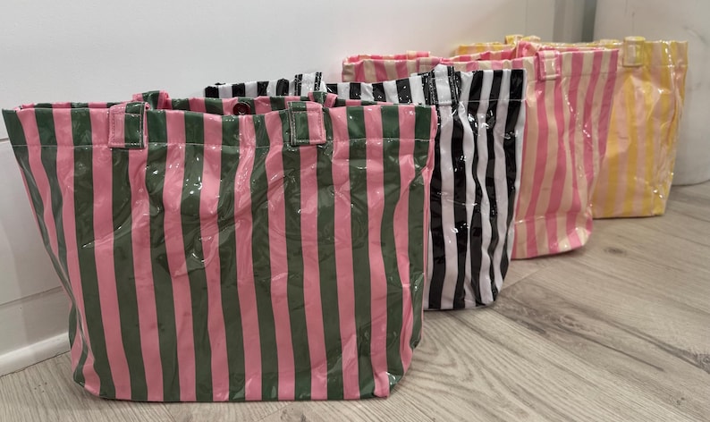 Puede incluir: Cuatro bolsas de mano con rayas verticales en varios colores: rosa y verde, blanco y negro, rosa y blanco y amarillo. Las bolsas tienen un acabado brillante y forma rectangular con asas.