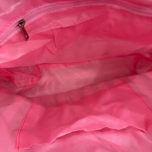 Puede incluir: Interior de un bolso tote rosa brillante con una cremallera en la parte superior y un bolsillo interior. La bolsa est&aacute; hecha de un material ligero, posiblemente nailon. El interior es de color rosa vibrante.