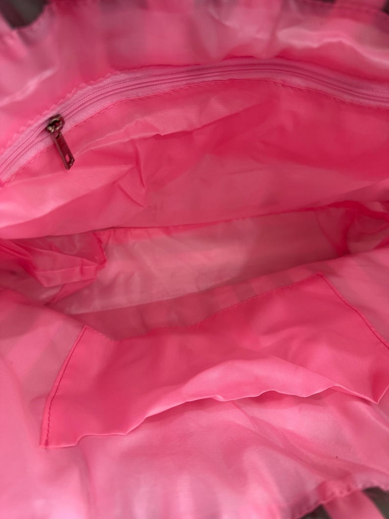 Puede incluir: Interior de un bolso tote rosa brillante con una cremallera en la parte superior y un bolsillo interior. La bolsa est&aacute; hecha de un material ligero, posiblemente nailon. El interior es de color rosa vibrante.