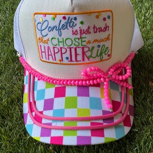 May include: White trucker hat with a colorful checkered brim and a pink beaded accent. The hat features a patch with the text "Confetti is just trash that CHOSE a much HAPPIER Life" in a rainbow of colors.
